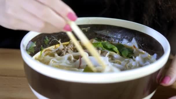 Een mooie jonge Aziatische meisje is het eten van Pho soep in een Aziatisch Cafe. Neemt noedels met Chinese eetstokjes. Chinees, Vietnamees of Japans café of restaurant. — Stockvideo