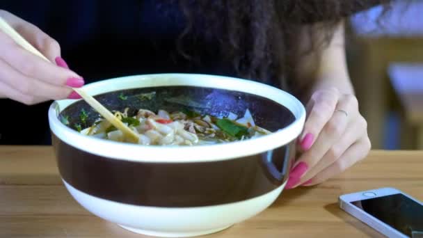 Uma linda jovem asiática tira uma foto de sopa de pho em um café asiático. Café ou restaurante chinês, vietnamita ou japonês — Vídeo de Stock