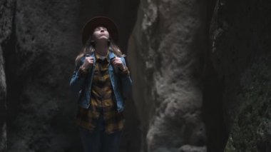 Bir mağara veya Kanyon kız gezgin. Şapka ve ceket giyiyor ve sırt çantası var. Bir antik mağara araştırıyor, macera arıyor. Dağ içinde dar bir yürüyüş yolu ile doğa yürüyüşü.