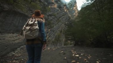 Dağlarda yürüyüş trekking. Dağ kanyonu boyunca bir sırt çantası ile yol boyunca yürüyen bir genç gezgin kadının arkasındaki arka görünümü. Bir antik mağara araştırıyor, macera arıyor