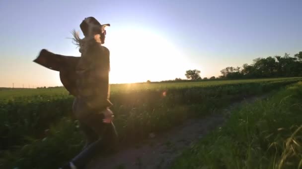 Kvinna bonden går längs vägen längs fältet. Känner en känsla av frihet från staden och närings livet. Engagerad i jordbruk. Iklädd en rusig skjorta och hatt. — Stockvideo