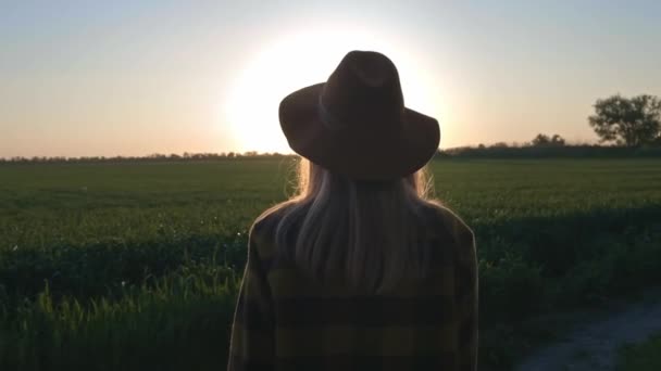 Una encantadora joven viajera o agricultora mira el atardecer o el amanecer. Usando camisa a cuadros y sombrero. Hermosa mujer despreocupada disfrutando de la naturaleza y la luz del sol en el campo de trigo al atardecer colorido increíble . — Vídeos de Stock