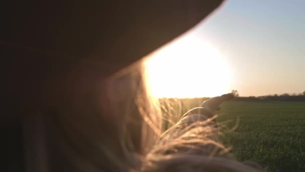 Το κορίτσι κοιτάζει τον ήλιο μέσα από το χέρι της. Γυναίκα που παίζει με τις ακτίνες του ήλιου. Ο ήλιος λάμπει μέσα από τα δάχτυλά της. Απολαμβάνει τη ζωή. Φορώντας ένα καρό πουκάμισο και καπέλο. — Αρχείο Βίντεο