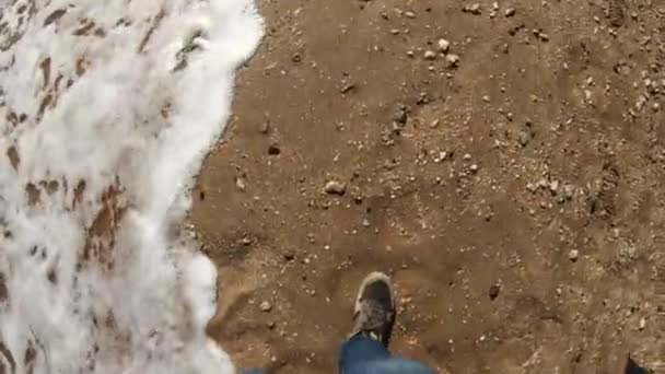 Uomo a piedi nudi sulla spiaggia di sabbia al rallentatore. Un uomo cammina lungo la costa lungo la spiaggia. Indossa scarpe da ginnastica estive. Scarpe imbevute di acqua salata. Passeggiate estive sul mare . — Video Stock