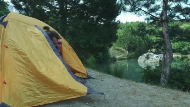 Jonge mannen wandelaar reiziger gaat langs de vijver. Op de back Marching rugzak. Een man loopt uit een tent in een groen bos in de buurt van het meer. Het concept van wandelen buitenactiviteiten. — Stockvideo