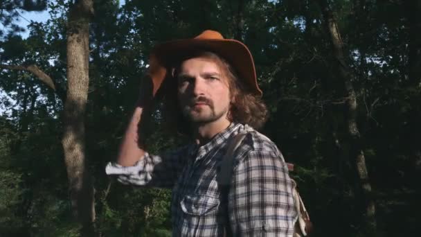 Un joven campesino caminando por el bosque. Senderismo en el bosque al atardecer. Estilo de vida activo. Llevando una camisa a cuadros y un sombrero de viajero. Viajero de mochila. Concepto de viaje de senderismo — Vídeos de Stock