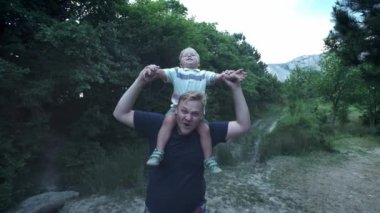 Mutlu genç baba oğlunu sırtında sırtında taşır ve yukarı bakar. Küçük çocuk, uçuşu taklit ederken babasının omuzlarında oturuyor..