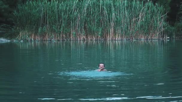 Молодой человек купается в зеленом озере. Купается в воде, наслаждается летом. Концепция отдыха на свежем воздухе . — стоковое видео