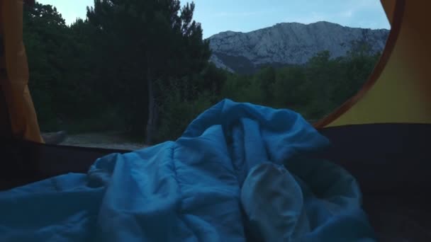 A young hiker guy stands near the tent, near the lake. Large forest spider. Active lifestyle. Wearing a checkered shirt and a travelers hat. Hiking travel concept. Success from the mountain lake. — Stock Video