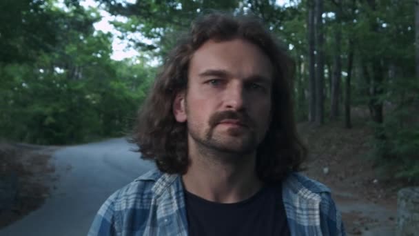 Portret: młody facet Hipster rzuca Longboard wokół szyi. Patrzy w aparacie. Znajduje się on w lesie. Młody człowiek z deskorolka na zewnątrz. — Wideo stockowe