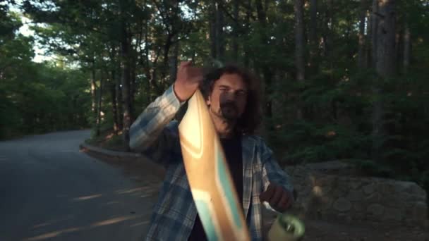 Young hipster in the forest, making fun with a longboard. Uses longboard as a guitar. Jumps like a rock star. Fun pastime on summer holidays. Slow motion shot. — Stock Video