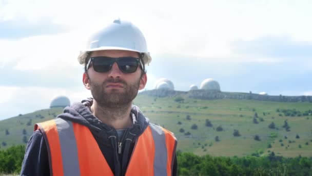 Erkek mühendis veya beyaz bir kask ve yelek içinde oluşturucu gözlük giyer. Yetiştiricilerin birkaç yarımkürenin arka planında. Yıldızları ve havayı izlemek. — Stok video