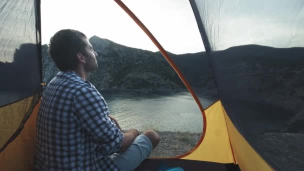 Um jovem está numa tenda de campismo. Faz uma foto em um smartphone. Fotografias uma bela paisagem . — Vídeo de Stock