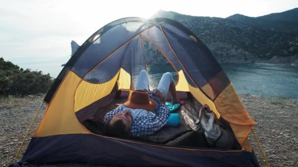 Close-up view of young couples legs lying in camping tent with feet joined while resting after hiking day. Happy lovers enjoying beautiful sea view and relaxing in the evening. — Stock Video