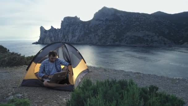 自由职业者男子工作使用笔记本电脑坐在海滩上的露营帐篷。自由职业者使用笔记本电脑和无线连接在新的创业项目。自由职业者暑期旅行 — 图库视频影像