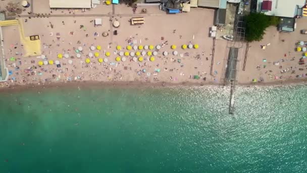 Antena: widok z góry na plażę. Ludzie kąpać się w morzu, na brzegu drewnianych parasoli plażowych — Wideo stockowe