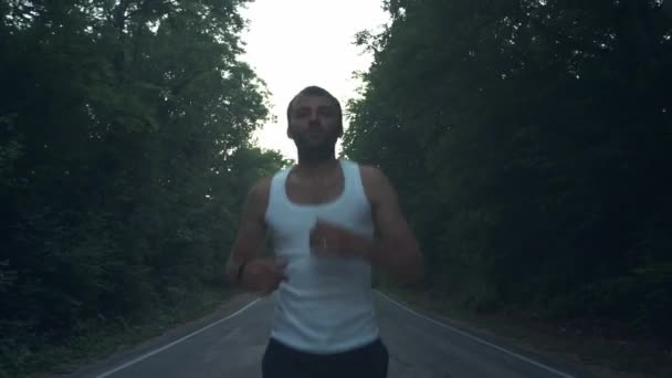 Un uomo che corre fuori nella natura la sera delle piogge. Maschio corridore facendo una corsa al crepuscolo su un'autostrada tra pini nella foresta. Impegnato in uno stile di vita sportivo attivo. Rafforza il tuo corpo. Sport nella natura — Video Stock