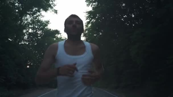 Hombre corriendo en la naturaleza en la noche lluviosa. Hombre corredor haciendo una carrera al atardecer en una carretera entre pinos en el bosque. Participó en un estilo de vida deportivo activo. Fortalece tu cuerpo. Deportes en la naturaleza — Vídeos de Stock