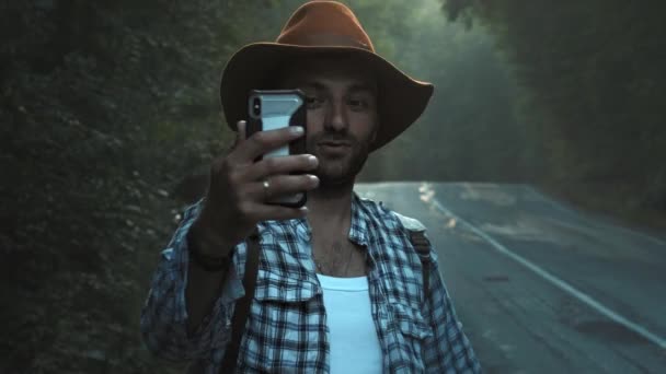 Um blogueiro de viagens grava vídeos para um blog. Caminhando pela estrada, segurando um smartphone em suas mãos. Faz um filme para o Vlog. Viagem viagem popular — Vídeo de Stock