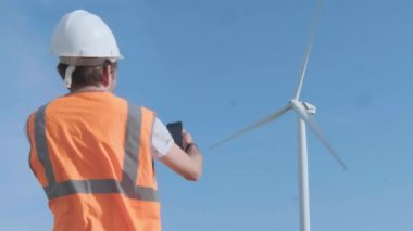 Bir erkek mühendis bir rüzgar türbini arka planda bir alanda bir akıllı telefon bir fotoğraf çeker. Rüzgar türbinini inceler. Çevre kirliliği kavramı, alternatif enerjinin yeni teknolojileri
