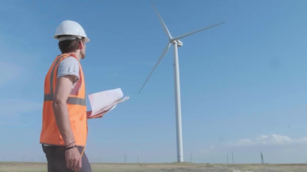 En manlig ingenjör fyller dokument i ett fält mitt i en vindturbin. Inspekterar vindkraftverket med en copter. Begreppet miljöförorening, ny teknik för alternativ energi — Stockvideo