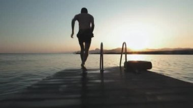 Genç milenyal otantik hipster adam muhteşem doğal c, temiz taze kelime ile dağ alp Gölü ahşap tahta üzerinde hızlı çalışır. komik bomba şekilde atlar. Yaz gezisi zevk alır.