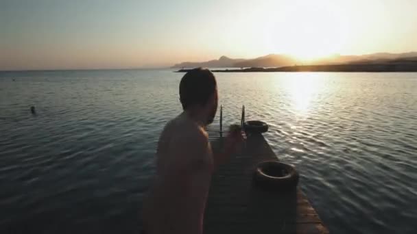 Jeune homme hipster millénaire authentique court rapidement sur la promenade en bois dans c naturel étonnant, lac alpin de montagne avec mot frais propre. saute dans la manière drôle de bombe. Obtient du plaisir du voyage d'été . — Video