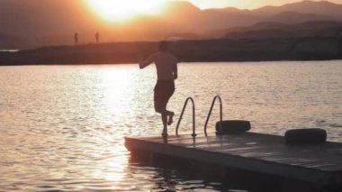 Genç milenyal otantik hipster adam muhteşem doğal c, temiz taze kelime ile dağ alp Gölü ahşap tahta üzerinde hızlı çalışır. komik bomba şekilde atlar. Yaz gezisi zevk alır.