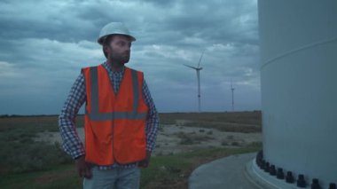 Portre: Rüzgar Türbinleri yakınında mühendis, ekolojik enerji geliştirmek. Çevre kirliliği kavramı, alternatif enerjinin yeni teknolojileri. Genel plan, akşam, bulutlu.