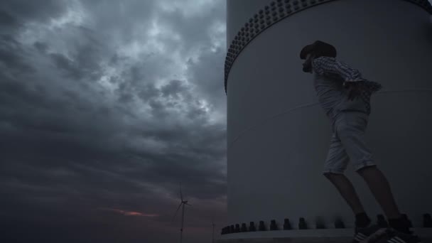 Ein junger Mann neben den Windrädern produziert ökologische Energie. das Konzept der Umweltverschmutzung, neue Technologien der alternativen Energien. Übersichtsplan, Abend, bewölkt. — Stockvideo