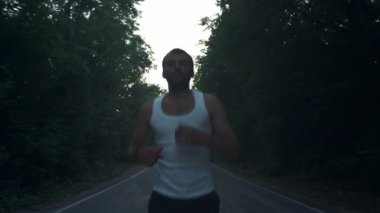 Yağmurlu akşamlarda doğada koşan bir adam. Erkek koşucu ormanda çam arasında bir otoyolda alacakaranlıkta bir çalışma yapıyor. Aktif bir spor yaşam tarzı meşgul. Vücudunuzu güçlendirir. Doğada spor