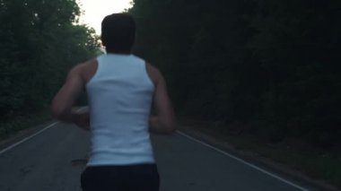 Yağmurlu akşamlarda doğada koşan bir adam. Erkek koşucu ormanda çam arasında bir otoyolda alacakaranlıkta bir çalışma yapıyor. Aktif bir spor yaşam tarzı meşgul. Vücudunuzu güçlendirir. Doğada spor