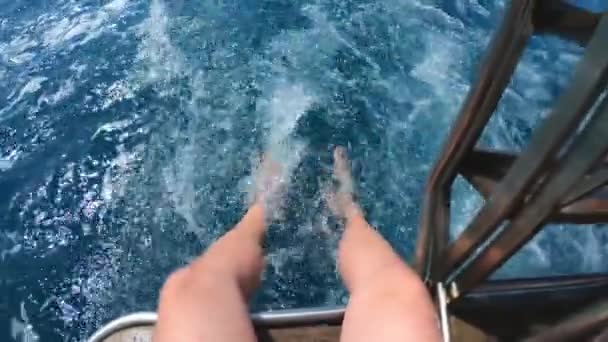 Schöner junger Mann sitzt mit den Beinen von einem Boot oder einer Jacht im Meer oder Ozean. spielt mit Wasser, fliegendem Spray. Sommerferien mit Freunden. Zeitlupe. — Stockvideo