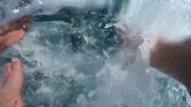 Yakışıklı genç adam deniz veya okyanusta bir tekne veya yat aşağı bacakları ile oturur. Suyla oynar, uçan sprey. Arkadaşlarınla yaz tatilleri. Yavaş çekim.