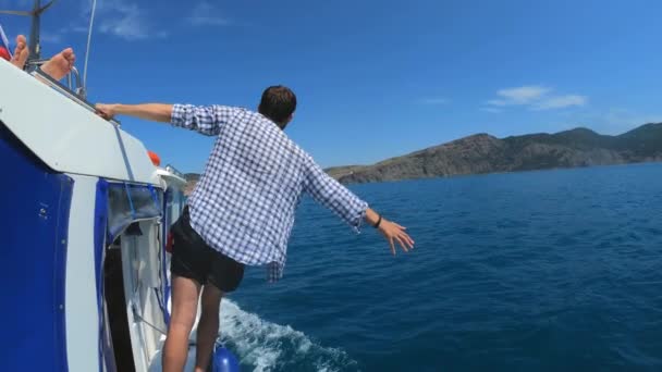 Un joven guapo está de pie en un barco o yate, flotando en el mar. Vacaciones de verano con amigos. Movimiento lento . — Vídeos de Stock