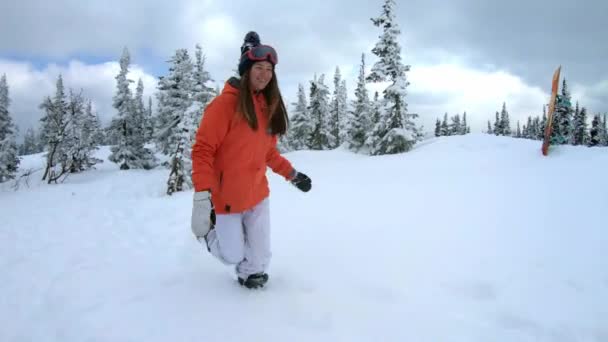 Alegre hermosa niña snowboarder corre en la nieve entre pinos nevados. Se arrodilla, arroja copos de nieve. Diversión invernal en la estación de esquí. cámara lenta, dolly shot . — Vídeos de Stock