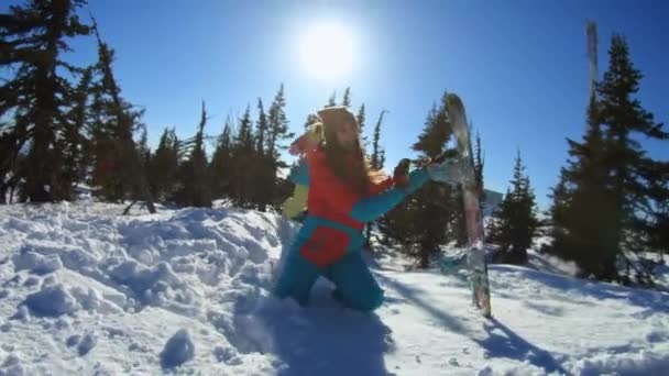 2人の陽気な美しい若い女の子のスノーボーダーやスキーヤーは、雪の流れで座って、笑顔で雪を投げるのを楽しんでいます。女性は冬の雪の松の中に立っています。スキー場での冬の楽しみ。スローモーション — ストック動画