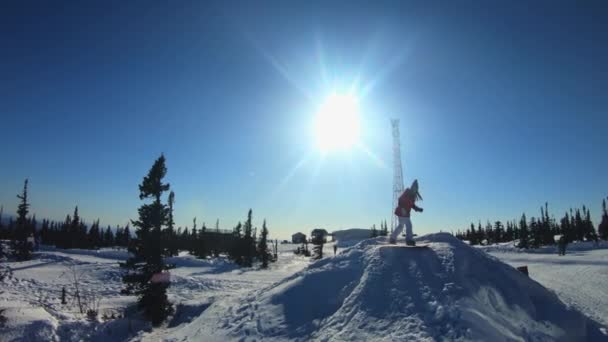 Vrolijke mooie jonge meid snowboarder doet een truc op een snowboard op een duikplank. Stuitert en valt in de sneeuw. Ritten op een winter plank. Winter pret in het skioord. Slow Motion, Dolly schot. — Stockvideo