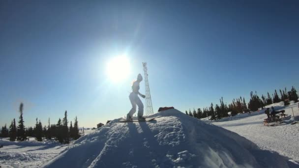 Vrolijke mooie jonge meid snowboarder doet een truc op een snowboard op een duikplank. Stuitert en valt in de sneeuw. Ritten op een winter plank. Winter pret in het skioord. Slow Motion, Dolly schot. — Stockvideo