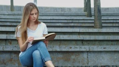 Parktaki genç güzel kız kitap okuyor. Bir öğrenci kitap okuyor, sayfaları çeviriyor. Beton üzerine oturur