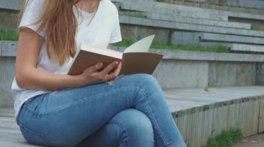 Parktaki genç güzel kız kitap okuyor. Bir öğrenci kitap okuyor, sayfaları çeviriyor. Beton üzerine oturur