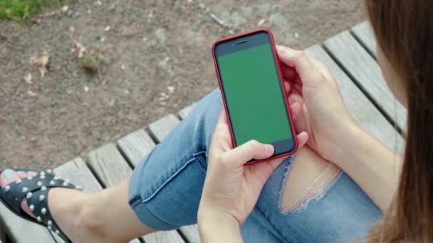 Belle fille tenant smartphone noir dans les mains d'un écran vert, main de femme tenant téléphone intelligent mobile avec écran vert clé chromatique, nouveau concept de technologie. Jeune belle fille dans le parc . — Video