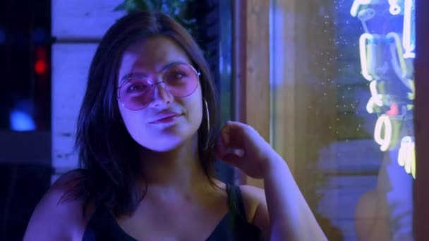 Jeune belle fille millénaire dans des lunettes redresse ses cheveux sur le fond de néons dans la rue — Video