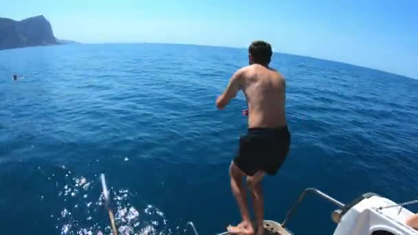 Beau jeune homme sautant d'un bateau ou d'un yacht dans la mer ou l'océan. Vacances d'été avec des amis. Les touristes s'amusent et plongent. Mouvement lent — Video