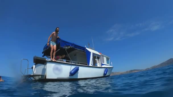 Pohledný mladík skáče z člunu nebo z jachty do moře nebo do oceánu. Letní prázdniny s přáteli. Turisté mají zábavu a potápění. Zpomaleně — Stock video