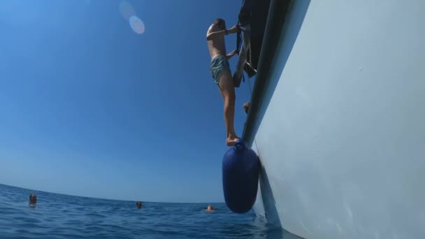 Guapo joven saltando de un barco o yate en el mar o el océano. Vacaciones de verano con amigos. Los turistas se divierten y bucean. Movimiento lento — Vídeos de Stock