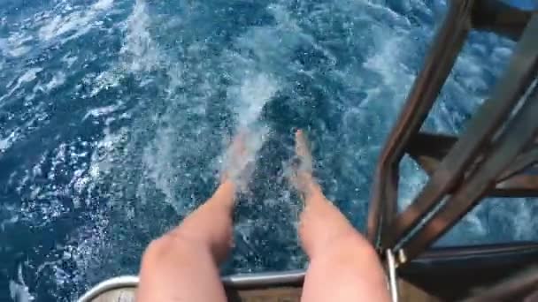 Pohledný mladík sedí s nohama dole na lodi nebo na jachtě v moři nebo v oceánu. Hraje s vodou, létající sprej. Letní prázdniny s přáteli. Zpomaleně. — Stock video
