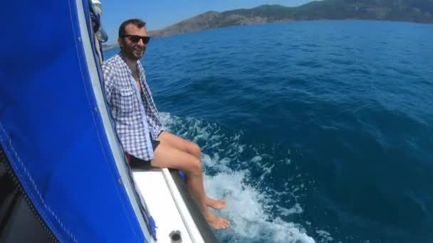 Guapo joven se sienta en un barco o yate, flota en el mar. Vacaciones de verano con amigos. Movimiento lento — Vídeo de stock