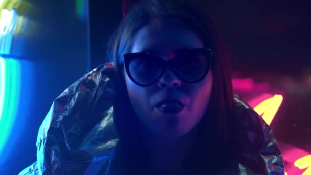 Menina adolescente moda jovem em óculos de pele soprando chiclete iluminado com rua neon azul rosa sinal, bela mulher milenar na moda noite luz brilho volta ao conceito dos anos 80 — Vídeo de Stock