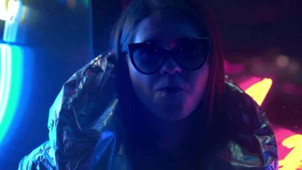 Young fashion teen girl in fur glasses blowing bubble gum illuminated with street neon blue pink sign, beautiful millennial woman in trendy night light glow back to 80s concept — Stock Video